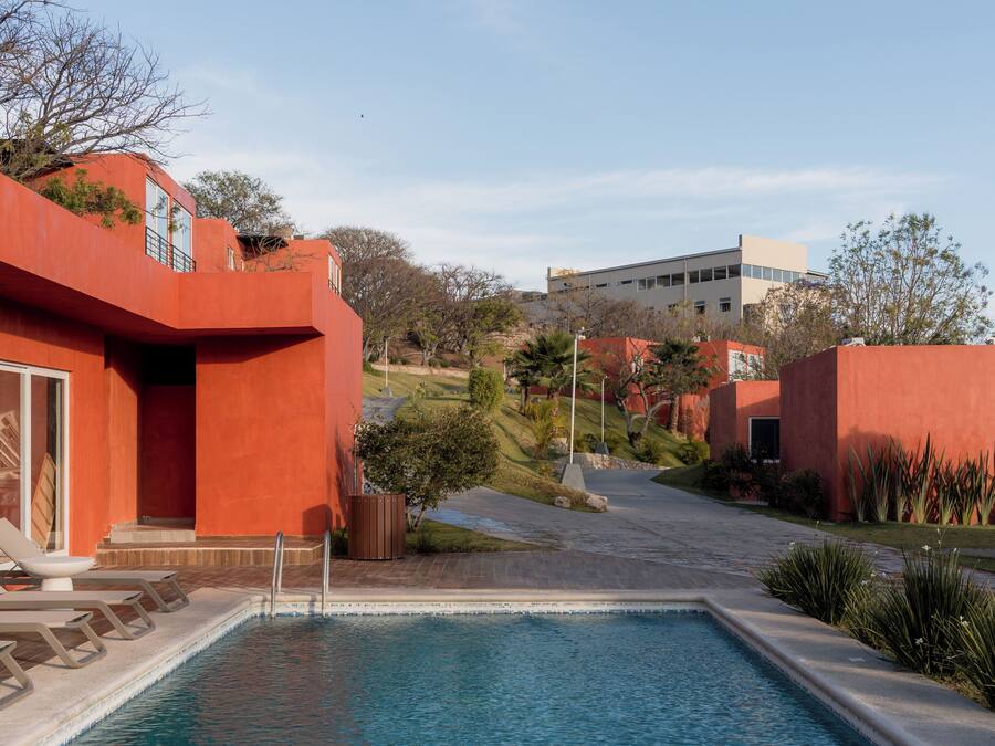 Una piscina con superficie de agua azul cristalina, rodeada de edificios rojos y un paisaje montañoso al fondo.