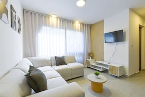 Un salon moderne avec un canapé d’angle, une table basse, un téléviseur à écran plat et une décoration minimaliste.