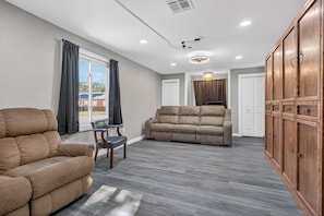 A spacious living area with a sofa, armchair, and wooden cabinet.