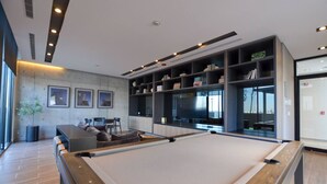 Une table de billard, un canapé et des fauteuils, une bibliothèque et une grande fenêtre.