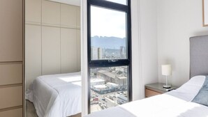 Une chambre d’hôtel avec une grande fenêtre, un lit, une table de chevet avec une lampe et une armoire.