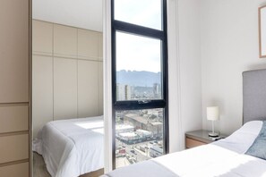 Ein Hotelzimmer mit einem großen Fenster, einem Bett, einem Nachttisch mit Lampe und einem Kleiderschrank.