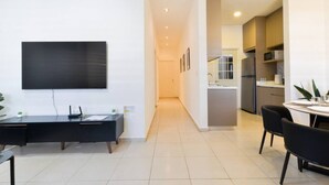 Quarto de hotel moderno com televisão de tela plana, uma escrivaninha com computador, área de refeições com cadeiras e cozinha equipada com geladeira e micro-ondas.