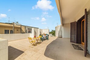 Eine Dachterrasse mit Tisch, Stühlen, einer Tür und Blick auf den Himmel.