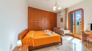 Quarto com cama, escrivaninha, cadeira, abajur, guarda-roupa e vista pela janela.