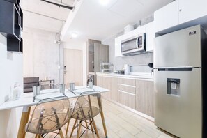 Une cuisine moderne équipée d’un réfrigérateur, d’un four à micro-ondes et d’un distributeur d’eau, tous en acier inoxydable. On y trouve une table à manger avec des chaises, ainsi qu’un petit coin salon avec un canapé.