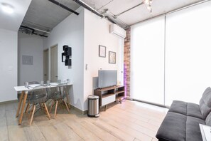 A modern living room with a dining area, a grey sofa, and a TV on a wooden stand. - ¡Boutique con Alberca y GYM! 5 personas + Wifi (Monterrey)