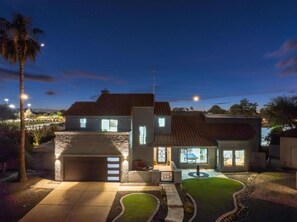 A two-story house with a garage, a well-lit driveway, and a small lawn. - Luxe Pickleball Villa by Glam Homes (Scottsdale)