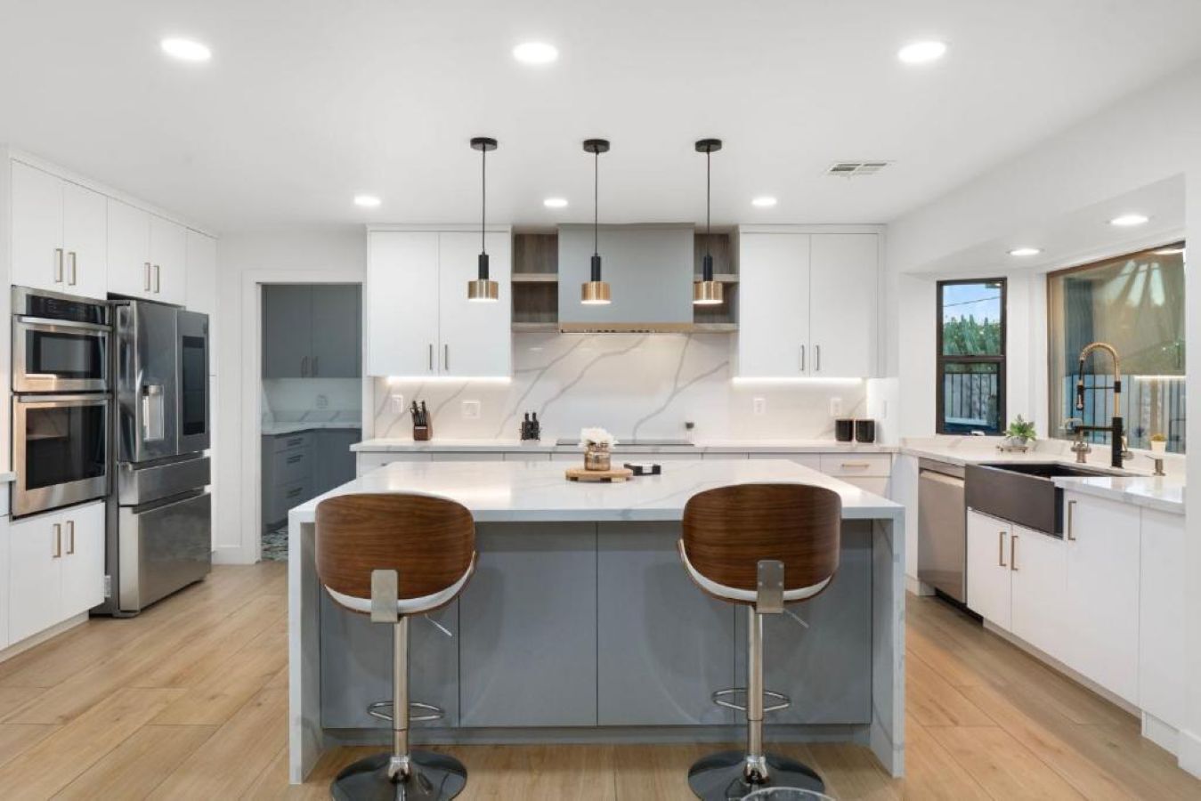 A modern kitchen with a central island, bar stools, stainless steel appliances, and pendant lighting.