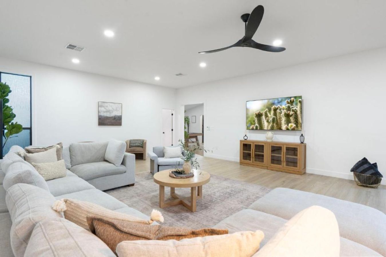 Ein modernes Wohnzimmer mit einem Ecksofa, einem Couchtisch, einem Deckenventilator, einem an der Wand montierten Fernseher und einem Holzkabinett.
