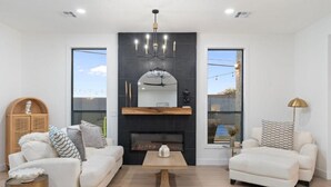 A modern living room with a fireplace, two sofas, a coffee table, and a large window. - Luxe Pickleball Villa by Glam Homes (Scottsdale)