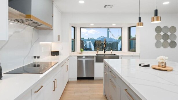 A modern kitchen with white cabinetry, stainless steel appliances, and a large window offering a view of a mountain. - Luxe Pickleball Villa by Glam Homes (Scottsdale)