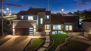A modern house with a garage, a well-maintained lawn, and a clear night sky. - Luxe Pickleball Villa by Glam Homes (Scottsdale)