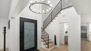A modern interior with a staircase, a glass door, and a kitchen in the background. - Luxe Pickleball Villa by Glam Homes (Scottsdale)