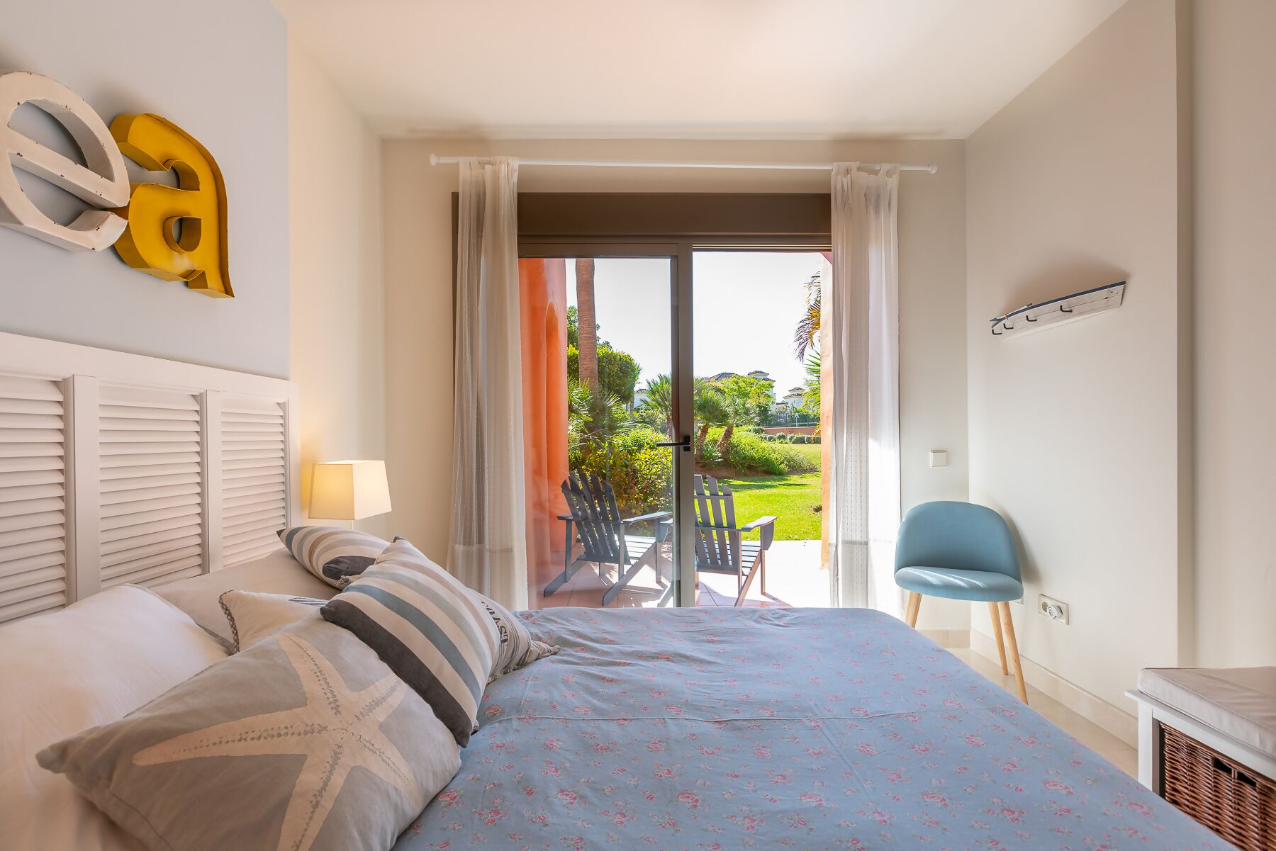 A bedroom with a bed, a chair, a balcony with a view, and a window with curtains.