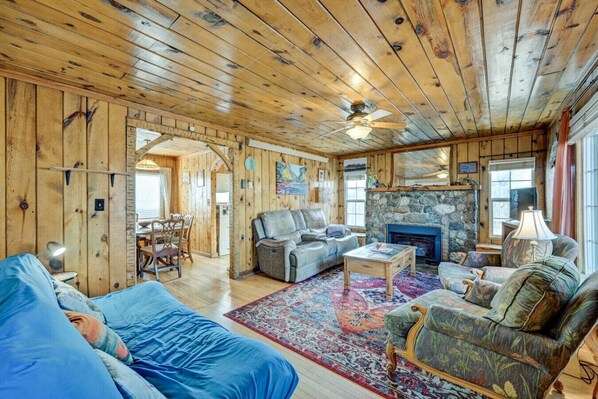 A log cabin interior with a fireplace, a ceiling fan, and a dining area.