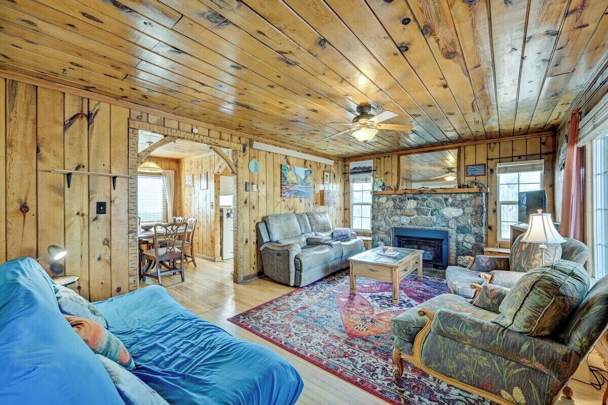 Interior acogedor de una cabaña con techo de madera, chimenea, comedor y sala de estar amoblada con un sofá y sillones.