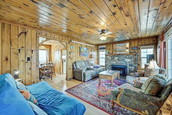 Ein gemütliches Blockhaus-Interieur mit Holzbalkendecke, Kamin, Essbereich und Wohnzimmer, möbliert mit einer Couch und Sesseln.