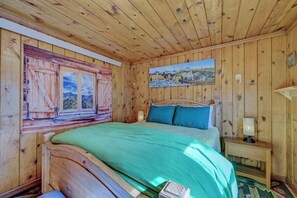 A wooden room with a bed, a painting, and a window with shutters. - The Cabin Down Below (Buena Vista)