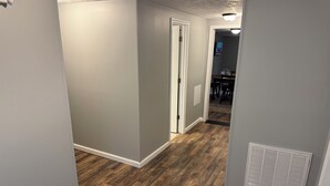 Un pasillo con suelo de madera, una puerta blanca y una rejilla de ventilación en la pared.