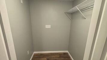 Un couloir étroit avec un plancher en bois, un mur de couleur gris clair et un luminaire au plafond.