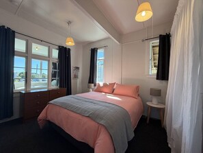 Een slaapkamer met een bed, twee bedlampen, een nachtkastje, een raam met gordijnen en uitzicht op het omliggende landschap.