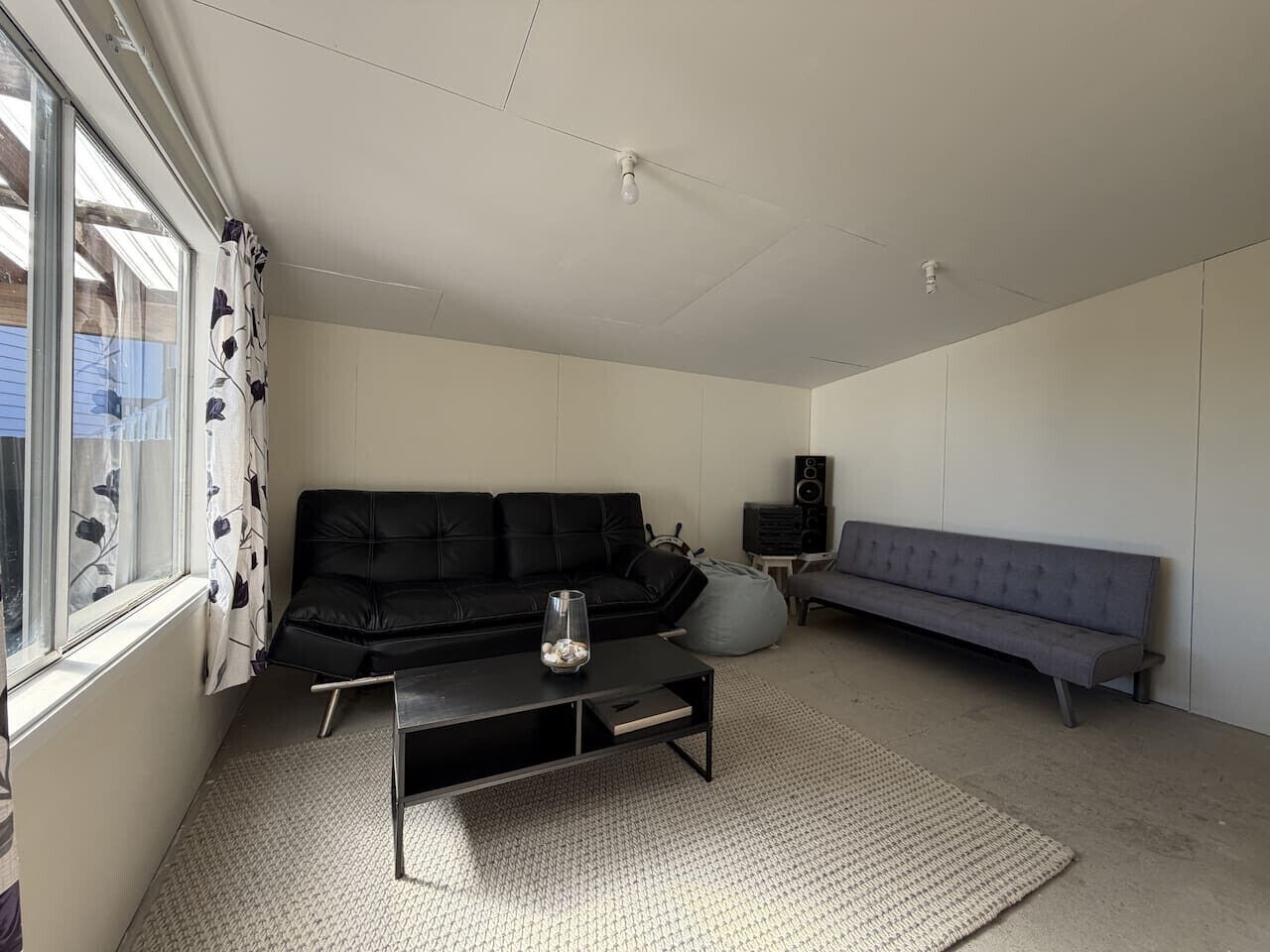 A living room with a black sofa, a grey sofa, a coffee table, and a speaker.