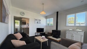Een woonkamer met een bank, fauteuil, televisie, tafel en open haard.