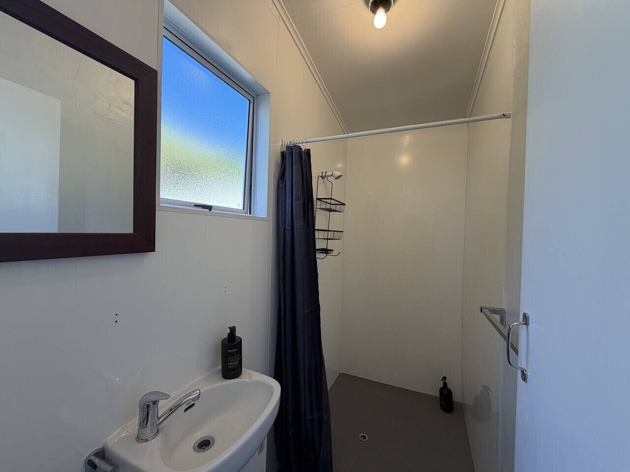 Ein kleines Badezimmer mit einem weißen Waschbecken, einem Fenster und einer Duschvorhang.