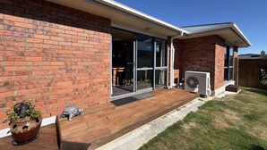 Fachada de ladrillo con terraza de madera, puerta corredera de vidrio y unidad de aire acondicionado.
