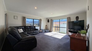 Un salón amplio con un sofá de cuero negro, un televisor de pantalla plana y un ventanal con vistas al exterior.