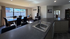 Una cocina moderna con una isla central, un comedor con sillas, una estufa integrada y vistas a través de amplias ventanas.