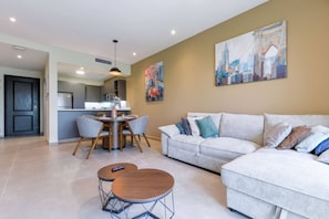 Uma sala de estar moderna com sofá, mesa de jantar com cadeiras, cozinha e um quadro na parede.