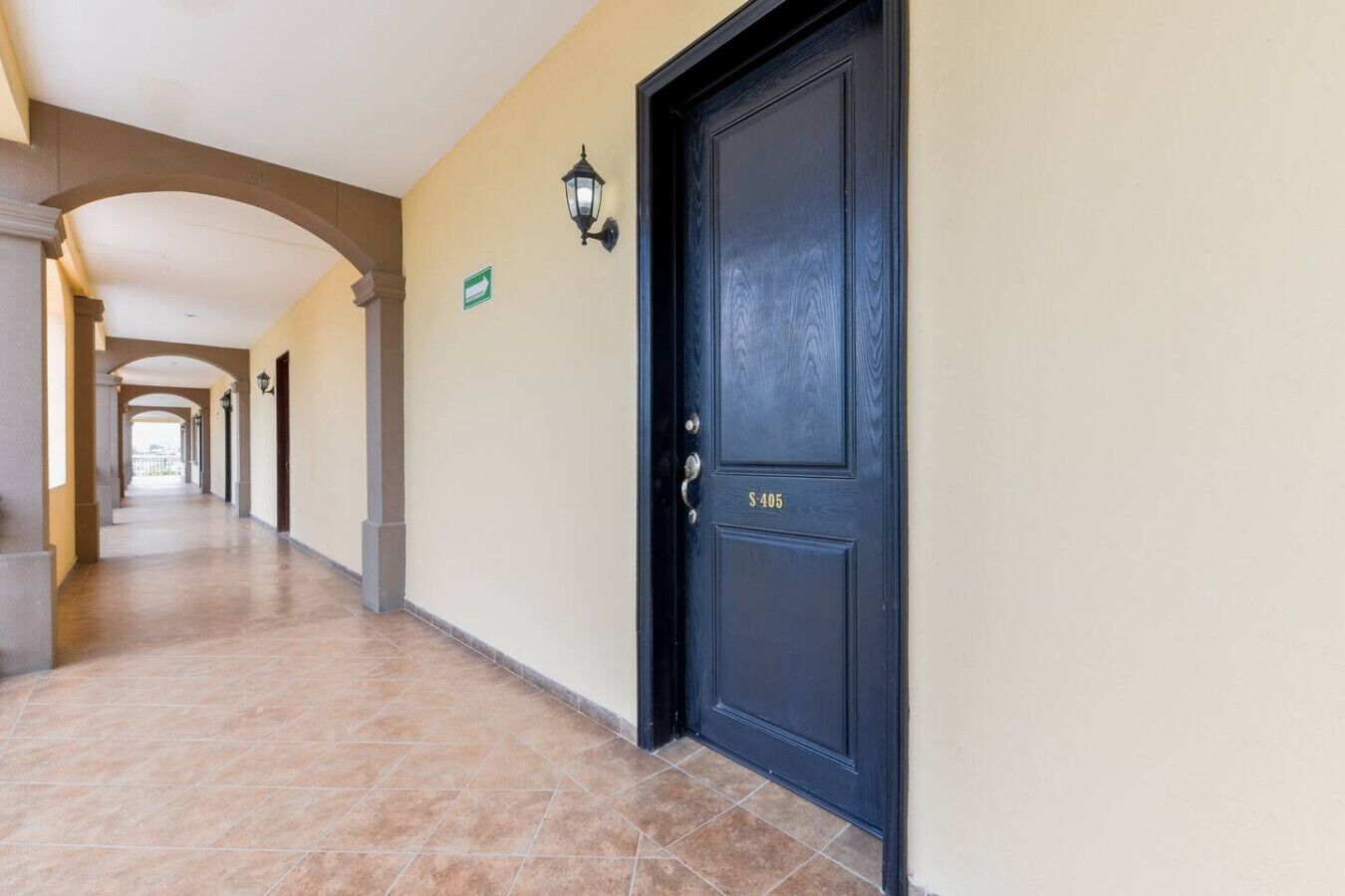 A corridor with a black door marked 'S-405,' beige walls, and a tiled floor.