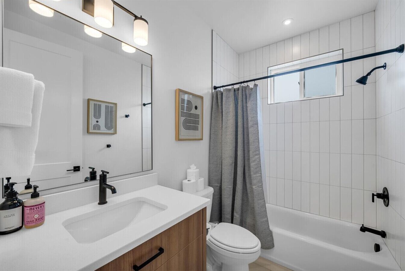 Ein modernes Badezimmer mit Waschbecken, Spiegel und Toilette in Weiß. Eine Dusche mit Duschvorhang und ein gerahmtes Bild an der Wand.
