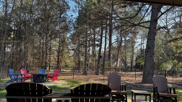 An outdoor patio with Adirondack chairs and tables, surrounded by a forested area. - SECaT Retreat:  Secluded 3-bedroom house in welcoming Holly Lake Ranch with AC (Holly Lake Ranch)