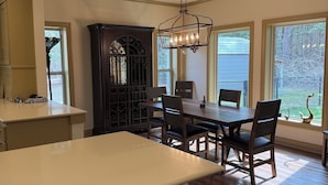 A dining area with a wooden table and chairs, a chandelier, and large windows. - SECaT Retreat:  Secluded 3-bedroom house in welcoming Holly Lake Ranch with AC (Holly Lake Ranch)