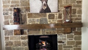 A stone fireplace with a deer painting above, a wooden shelf below, and a bear sculpture to the left. - SECaT Retreat:  Secluded 3-bedroom house in welcoming Holly Lake Ranch with AC (Holly Lake Ranch)