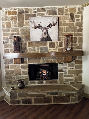 A stone fireplace with a deer painting above, a wooden shelf below, and a bear sculpture to the left. - SECaT Retreat:  Secluded 3-bedroom house in welcoming Holly Lake Ranch with AC (Holly Lake Ranch)