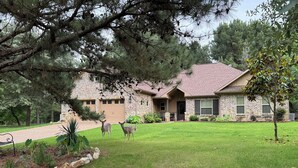 A stone house with a brick driveway, a lawn, and two deer in the yard. - SECaT Retreat:  Secluded 3-bedroom house in welcoming Holly Lake Ranch with AC (Holly Lake Ranch)