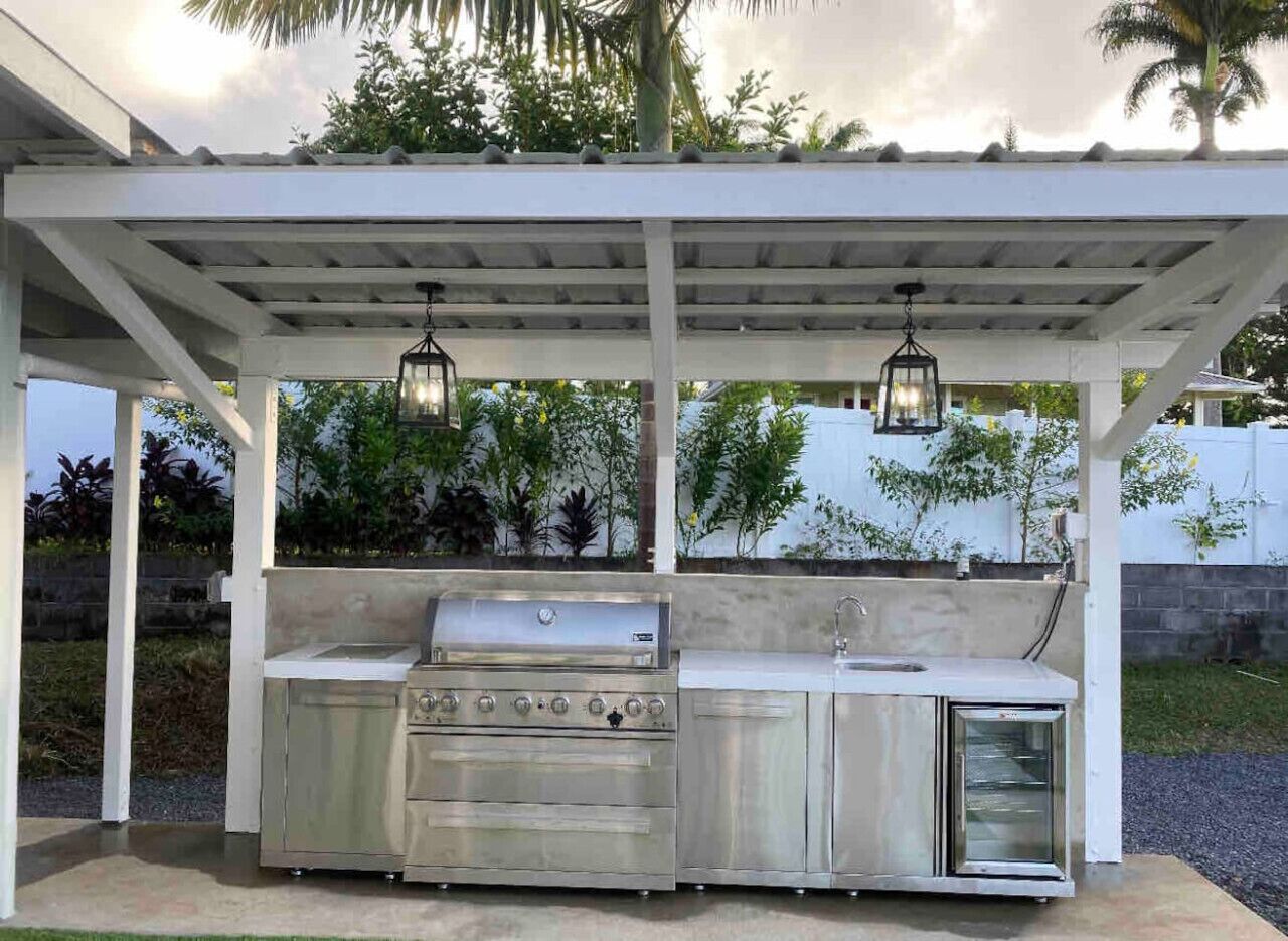 Een buitenkeuken met een barbecue, spoelbak en hangende lantaarns onder een pergola.