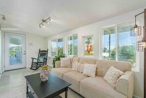 A modern living room with a beige sofa, a dark wooden coffee table, and a rocking chair. - Akaka Falls 6BR Ocean‑View Retreat with Hot Tub (Honomū)