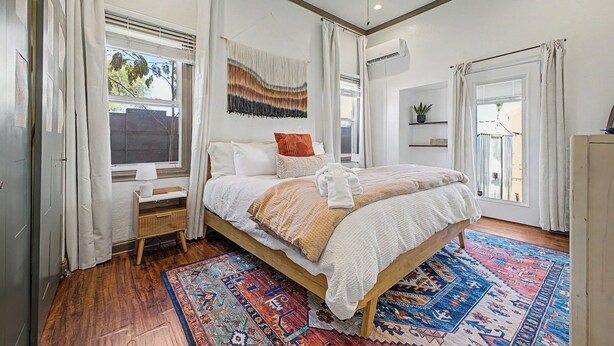 Une chambre à coucher comprenant un lit, une table de chevet, une fenêtre, un ventilateur de plafond et un tapis à motifs.