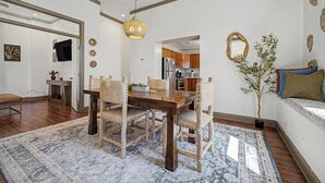 Un coin repas avec une table et des chaises en bois, un luminaire suspendu et une cuisine en arrière-plan.