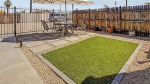 Une cour arrière clôturée avec une table et des chaises de patio, une petite pelouse et une clôture en bois.