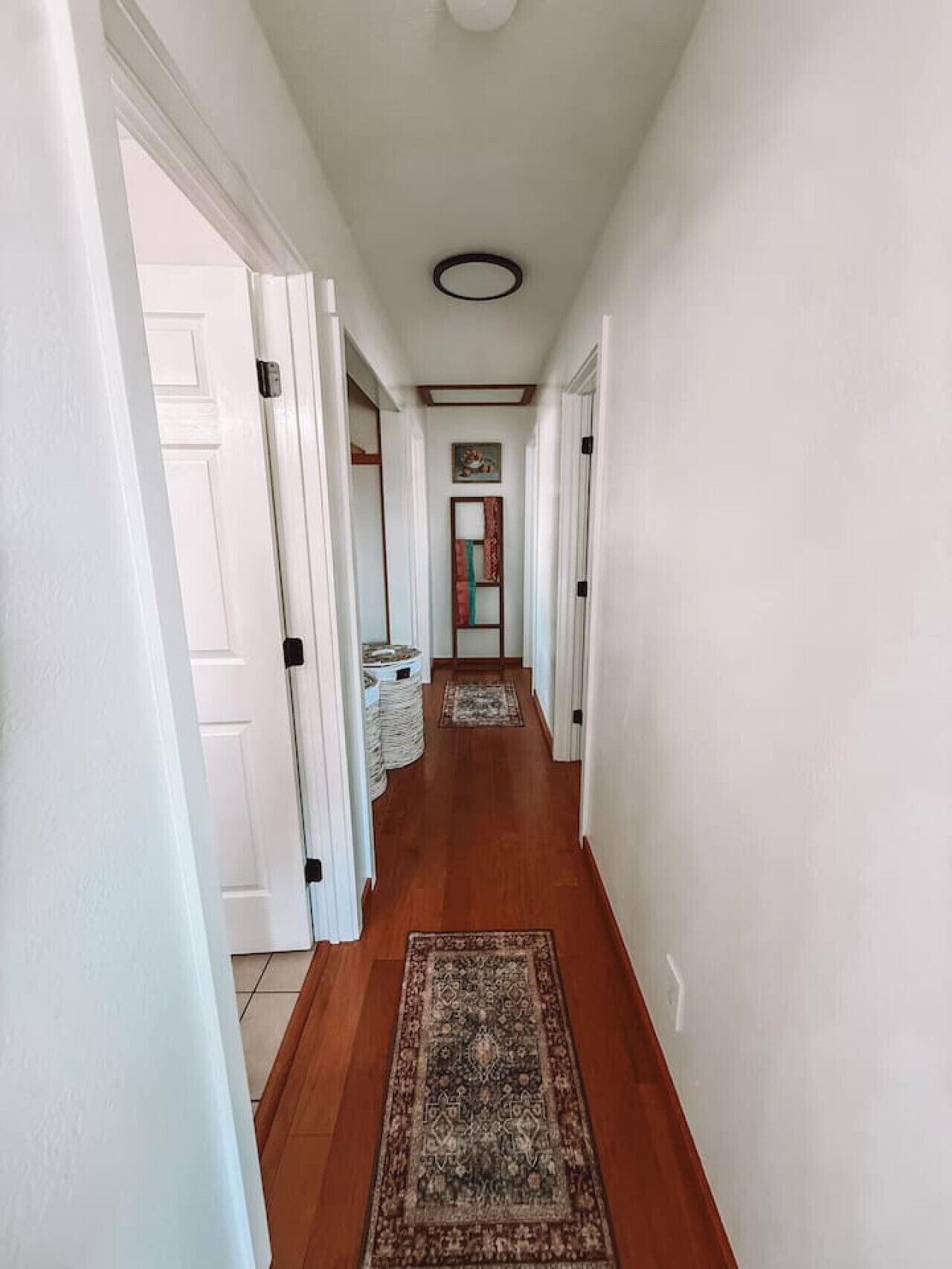 A hallway with wooden flooring, white walls, and a ceiling light fixture.