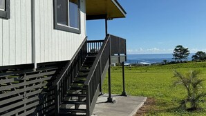 Ein Gebäude mit einer Holztreppe, die zu einer überdachten Veranda führt, mit Blick auf das Meer und einem grünen Feld im Hintergrund.