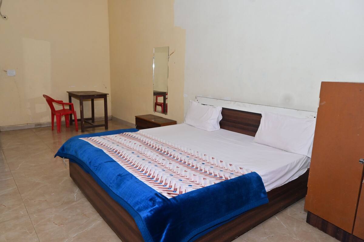 A hotel room with a bed, a desk, a chair, a wardrobe, and a mirror.