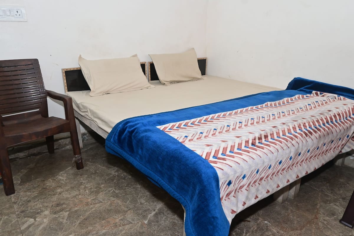 A single bed with a patterned bedspread, a wooden chair, and a tiled floor.