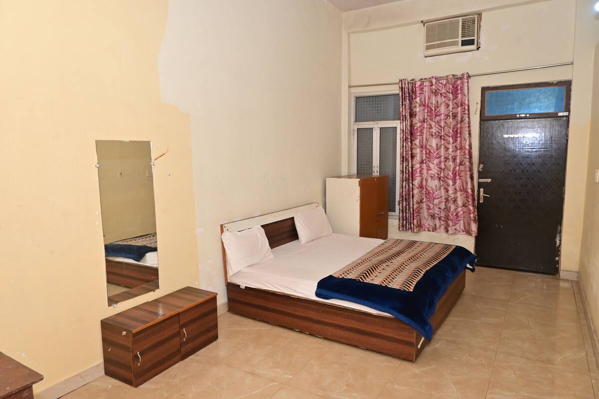 A bedroom with a bed, a wardrobe, a mirror, a door, and a window with curtains.